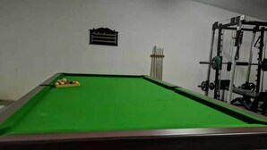 A pool table with balls, a wall-mounted rack, and a weightlifting station.