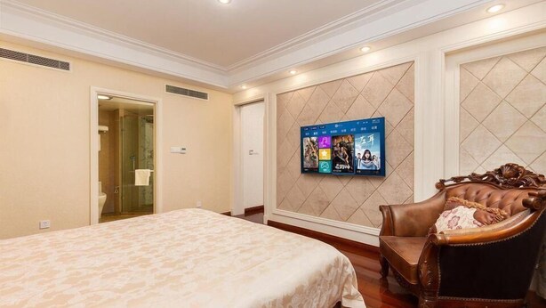 A hotel room with a large bed, a television mounted on the wall, and a classic armchair. - Greentree Inn Nantong Haimen Sanchang North Wangjiang Road Business Hotel (Nantong)