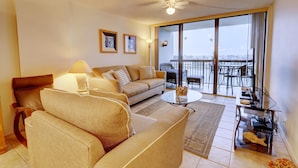 A living room with a sofa, a coffee table, and a balcony with a view. - St Pete Beach Yacht and Tennis Club 90 Day Rental Gated With Pool (St. Pete Beach)