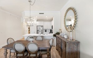 Un comedor con una mesa y sillas de madera, una cocina al fondo y un espejo decorativo en la pared.