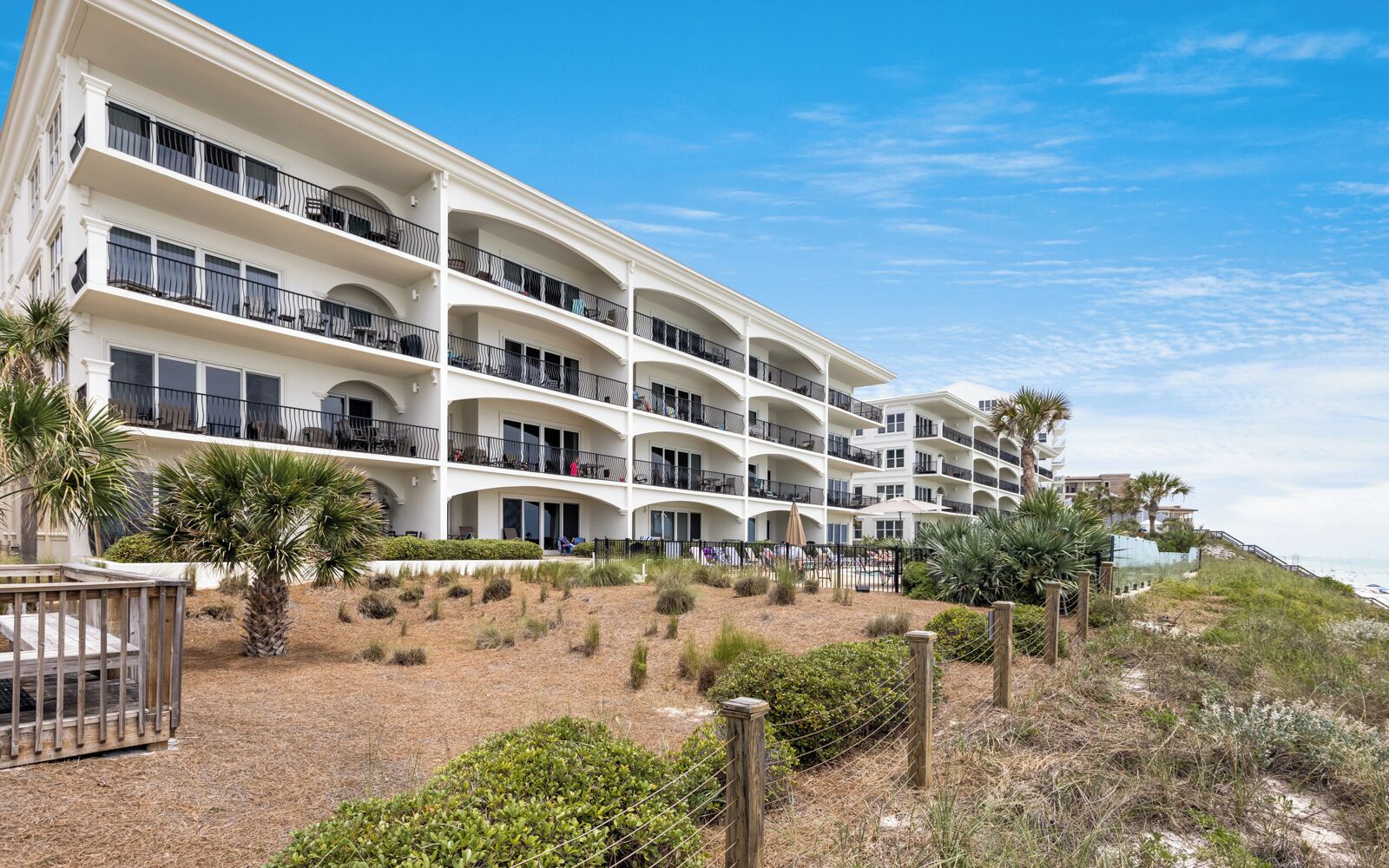 A multi-story hotel with balconies, a sandy landscape, and palm trees.