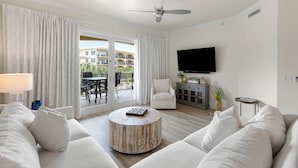 A modern living room with a sofa set, a round coffee table, a TV mounted on the wall, and a balcony with outdoor furniture. - Resort Style Community - Private Beach Access (Santa Rosa Beach)