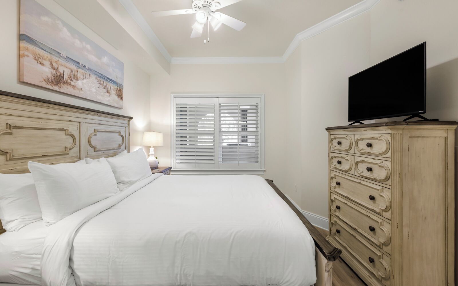 A hotel room with a large bed, a dresser, a television, and a window with blinds.