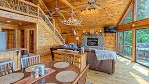 A wooden cabin interior with a dining area, fireplace, and large windows. - Hot Tub, 3 Fireplaces, Mountain Views, Game Room (Blue Ridge)