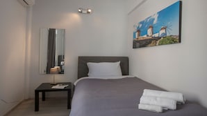 A bedroom with a bed, a nightstand, a lamp, a painting of windmills, and a mirror. - Lux 2BR Home On The Steps Of Acropolis (Athens)
