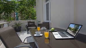 A balcony with a table set for breakfast, including a laptop, drinks, and fruit. - Lux 2BR Home On The Steps Of Acropolis (Athens)