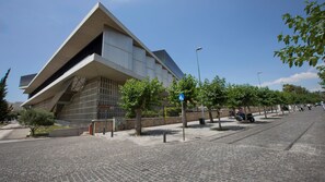 A modern building with a unique triangular roof and a paved street with trees and a few parked motorcycles. - Lux 2BR Home On The Steps Of Acropolis (Athens)