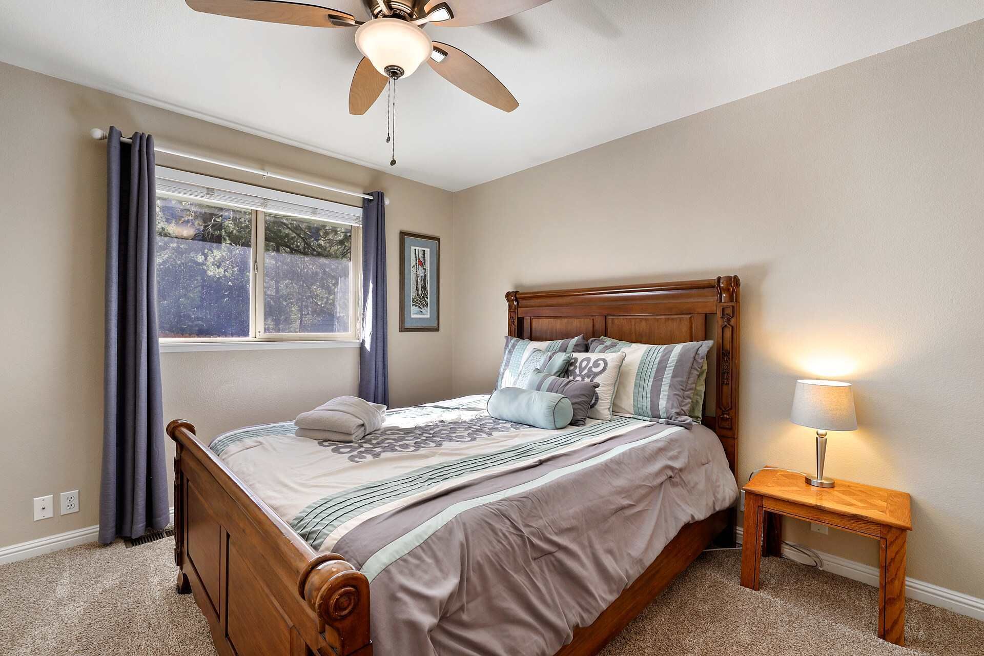 Une chambre à coucher avec un lit en bois, un ventilateur de plafond, une lampe de chevet et une fenêtre avec des rideaux.