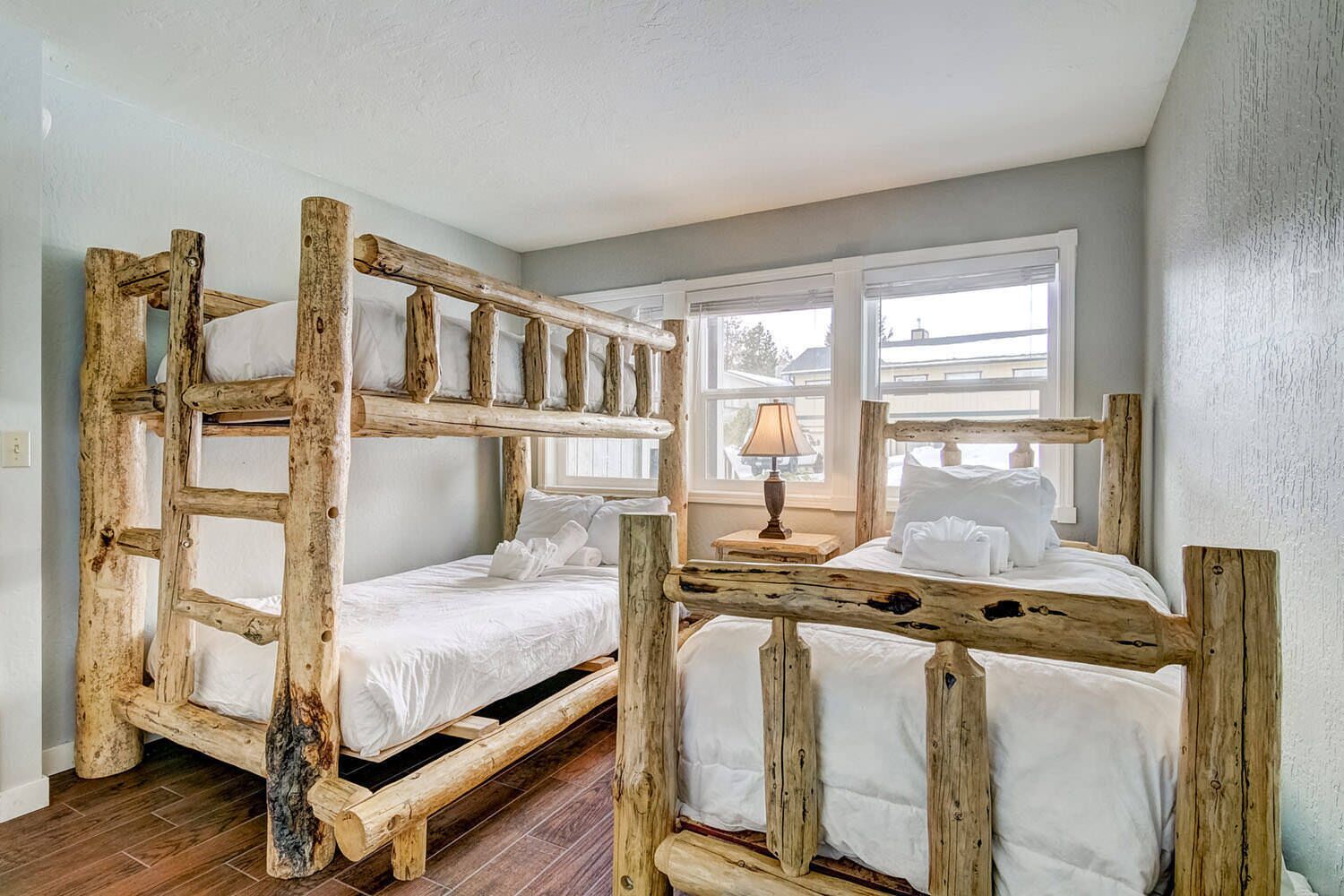 Una habitación con dos literas de madera natural, ropa de cama blanca y una ventana con persianas.