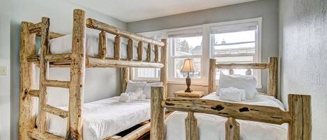 Una habitación con dos literas de madera natural, ropa de cama blanca y una ventana con persianas.
