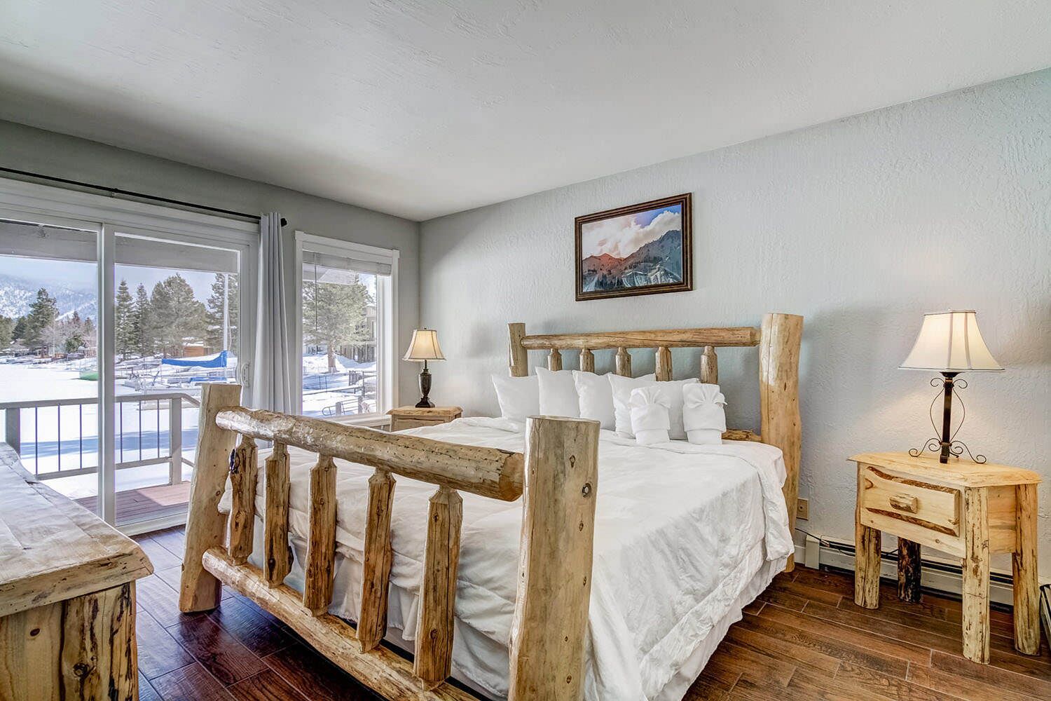 A bedroom with a wooden bed, two bedside tables, a window with a view of a snowy landscape, and a painting on the wall.
