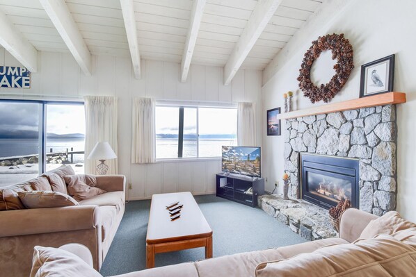 A living room with a stone fireplace, a television, and a view of the sea.