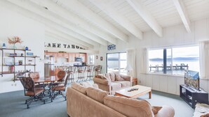 A spacious living room with a large window overlooking a lake, a kitchen area, and a cozy seating arrangement. - Waters Edge Vista HOA Pool & Pier Access (Tahoma)