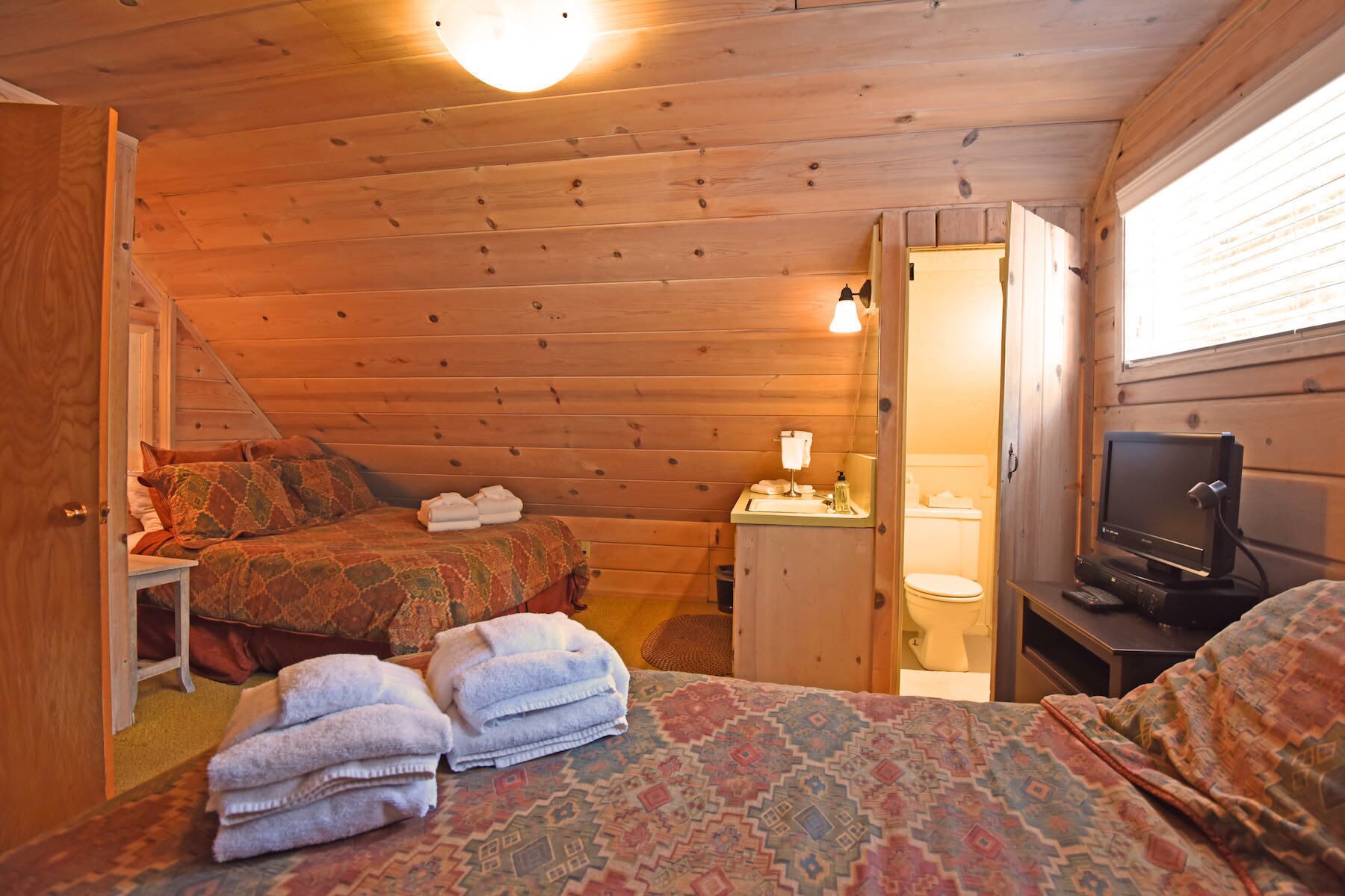 A cozy cabin room with two beds, a small bathroom, and a television.
