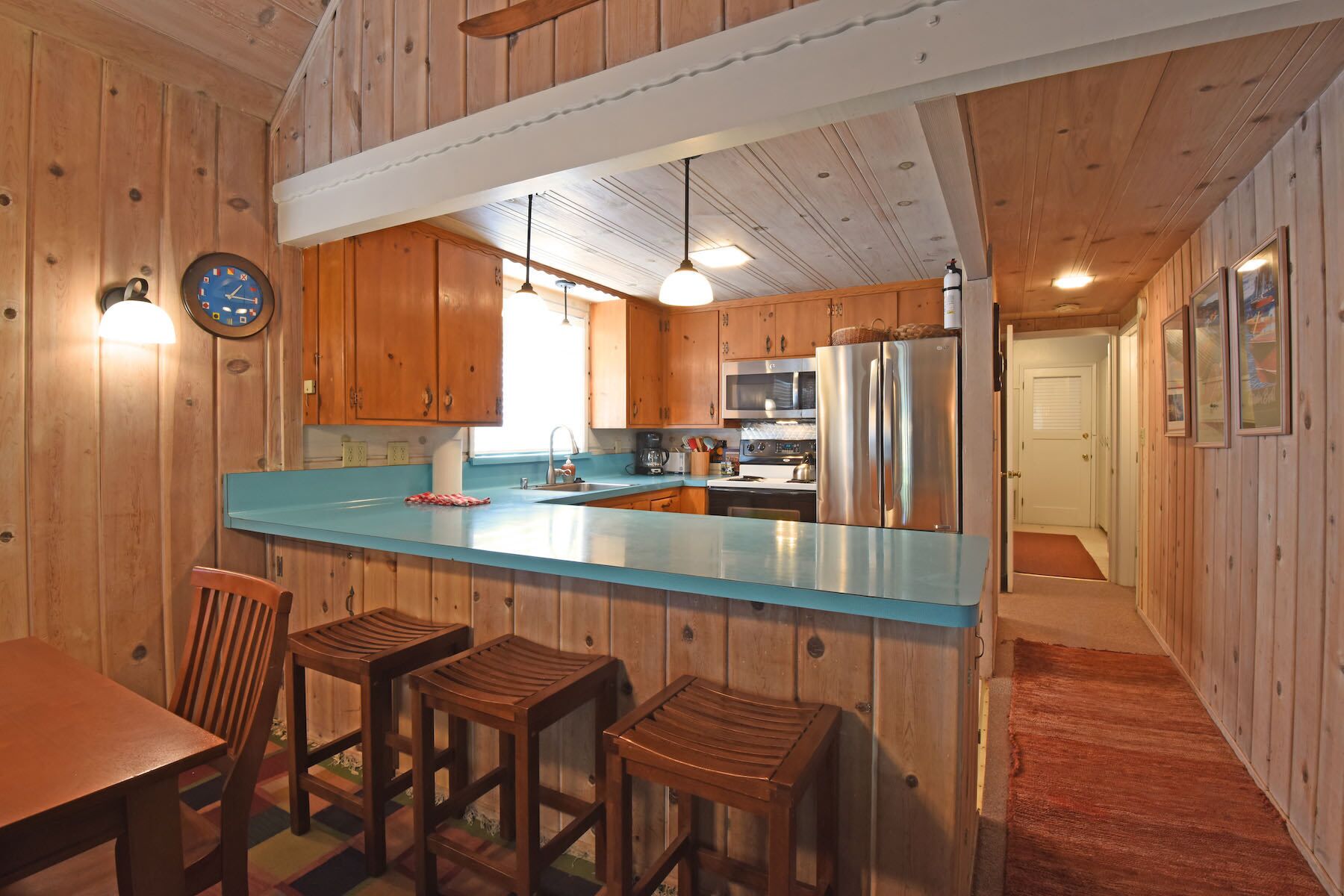 A kitchen with wooden cabinets, a blue countertop, a stainless steel refrigerator, and a dining area with stools.