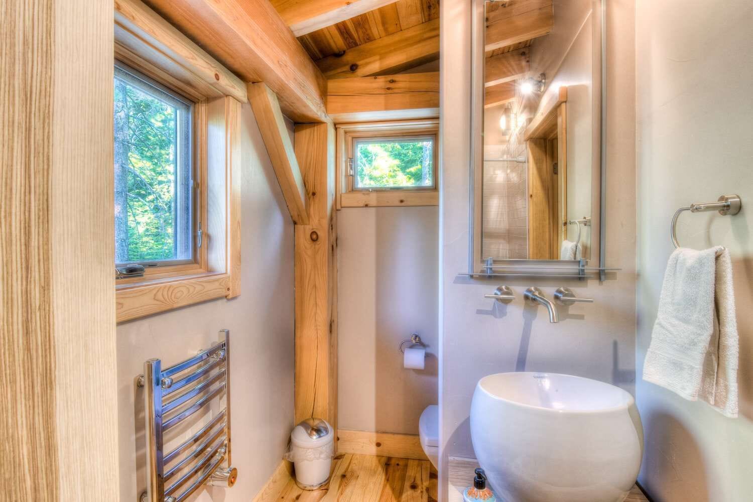 Un baño compacto con techo de madera, un ventanal grande, un lavamanos y un espejo.