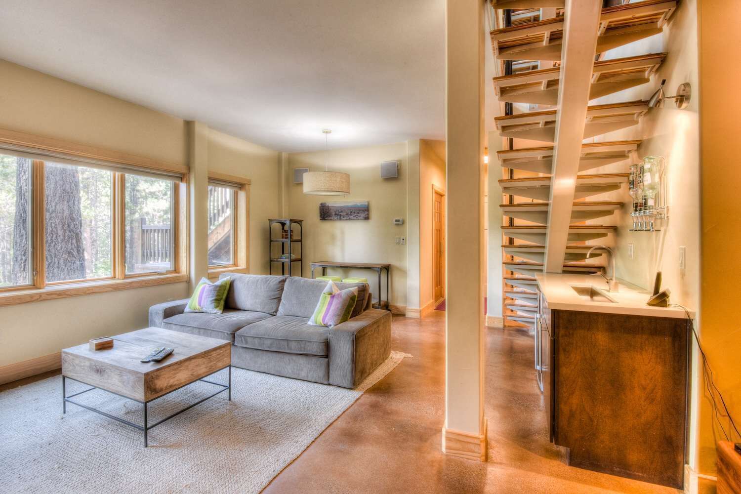 A modern living room with a grey sofa, a coffee table, and a staircase with bookshelves.