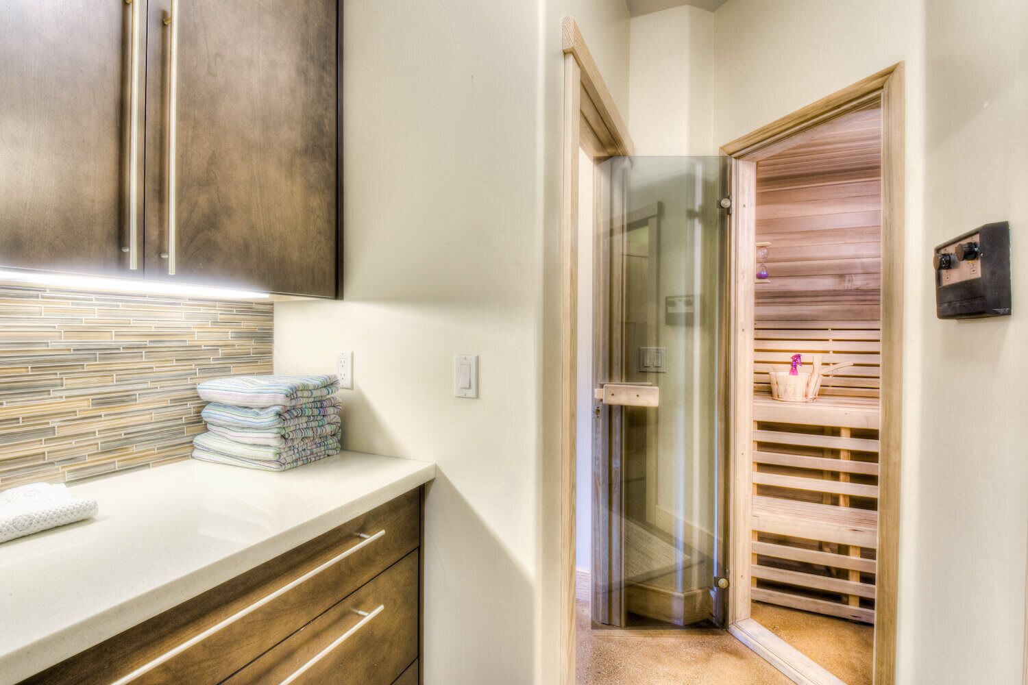 A modern bathroom with a glass shower enclosure, a wooden vanity, and a towel stack.