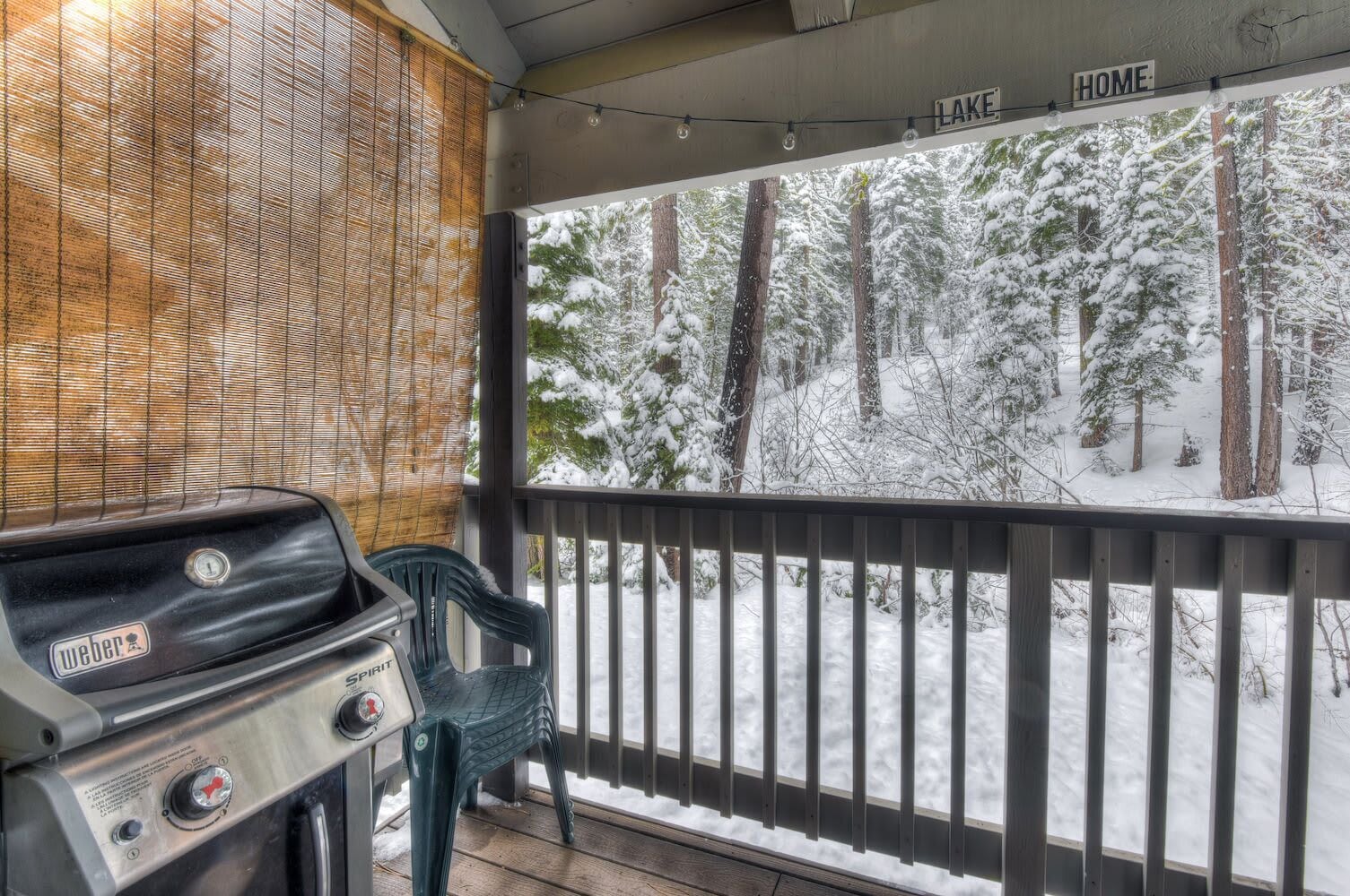 A covered outdoor area with a grill, a chair, and a view of a snowy forest.