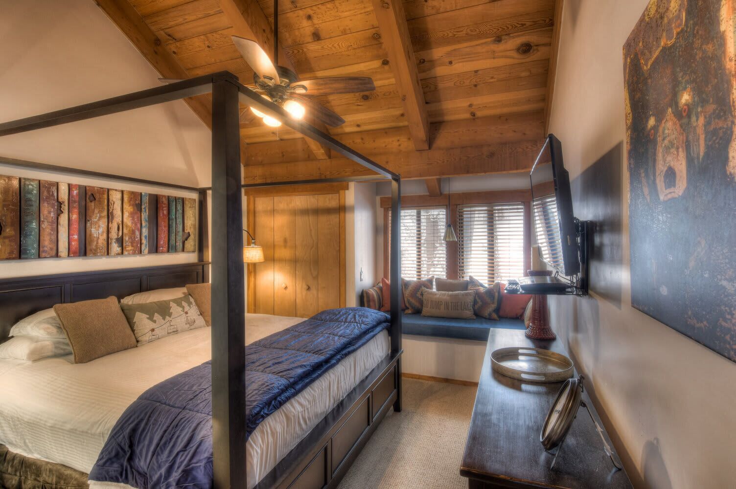 Un lit à baldaquin, un plafond en bois, un banc de fenêtre agrémenté de coussins et un radiateur fixé au mur.