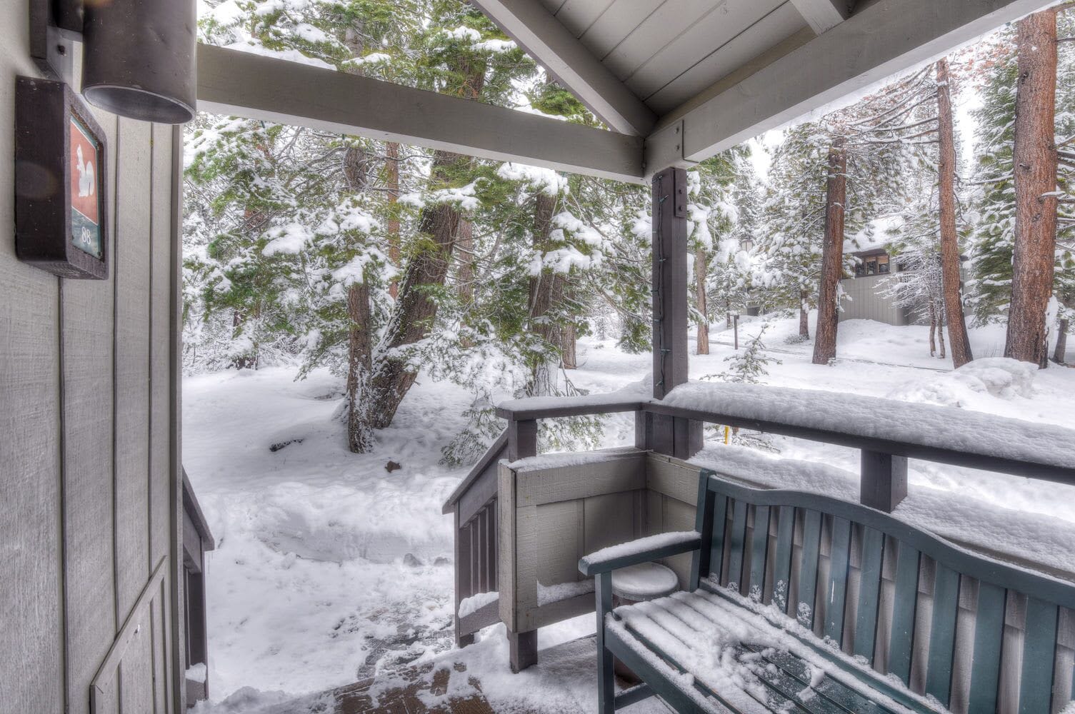 A covered porch with a bench, surrounded by snow-covered trees.
