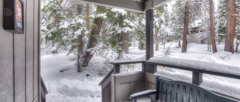 A covered porch with a bench, surrounded by snow-covered trees.