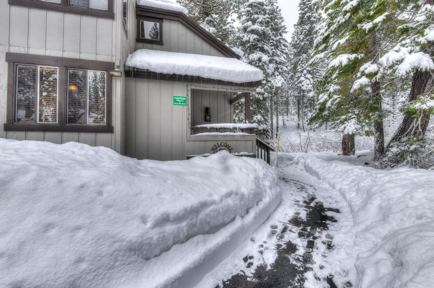 Un bâtiment recouvert de neige, sur lequel on peut voir un panneau indiquant « ATTENTION », un autre panneau indiquant « BIENVENUE » et un chemin menant à l’entrée.