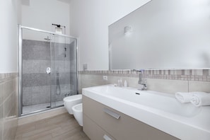 Un baño moderno con ducha de vidrio, lavamanos blanco y un espejo grande.