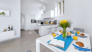 A modern kitchen with white cabinetry, a dining area with a blue table mat, and breakfast items like croissants and orange juice. - Villa Anna with private Terrace and Sea View (Positano)