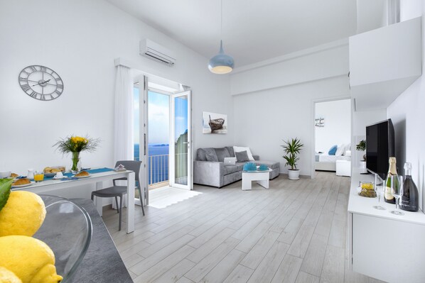 Una sala de estar moderna con sofá, un comedor con mesa y sillas, televisor y un balcón con vistas.
