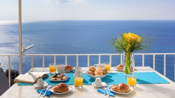 A table set with breakfast items, a vase of flowers, and a view of the sea. - Villa Anna with private Terrace and Sea View (Positano)
