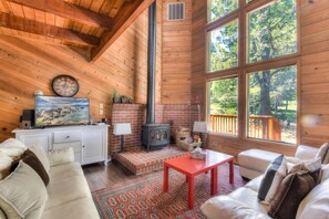A cozy cabin interior with a fireplace, large windows, a white cabinet, and a comfortable seating area. - Northwoods Hangout Near Tahoe Donner (Truckee)