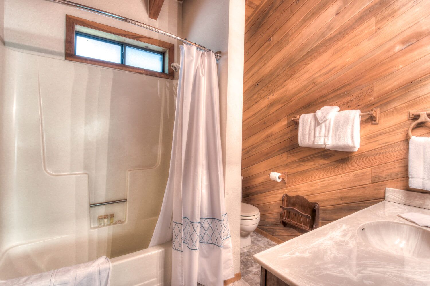 Un bagno con soffitto in legno, una vasca, una tenda da doccia, un water e un lavandino.