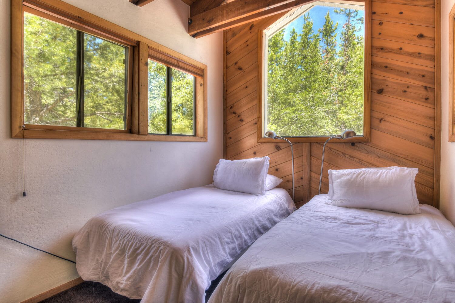 A room with two beds, large windows, and wooden walls.