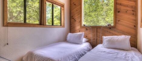 A room with two beds, large windows, and wooden walls.