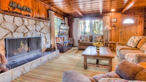 A cozy cabin interior with a stone fireplace, wooden walls, a comfortable sofa, and a television.