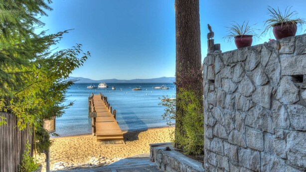 A wooden pathway leading to a beach with a stone wall and potted plants.