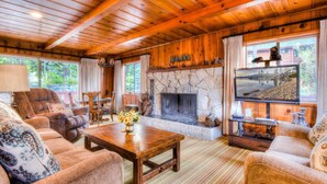 A cozy cabin interior with a stone fireplace, wooden furniture, and a television.