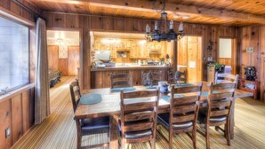 A wooden cabin interior with a dining area, kitchen, and a large window.