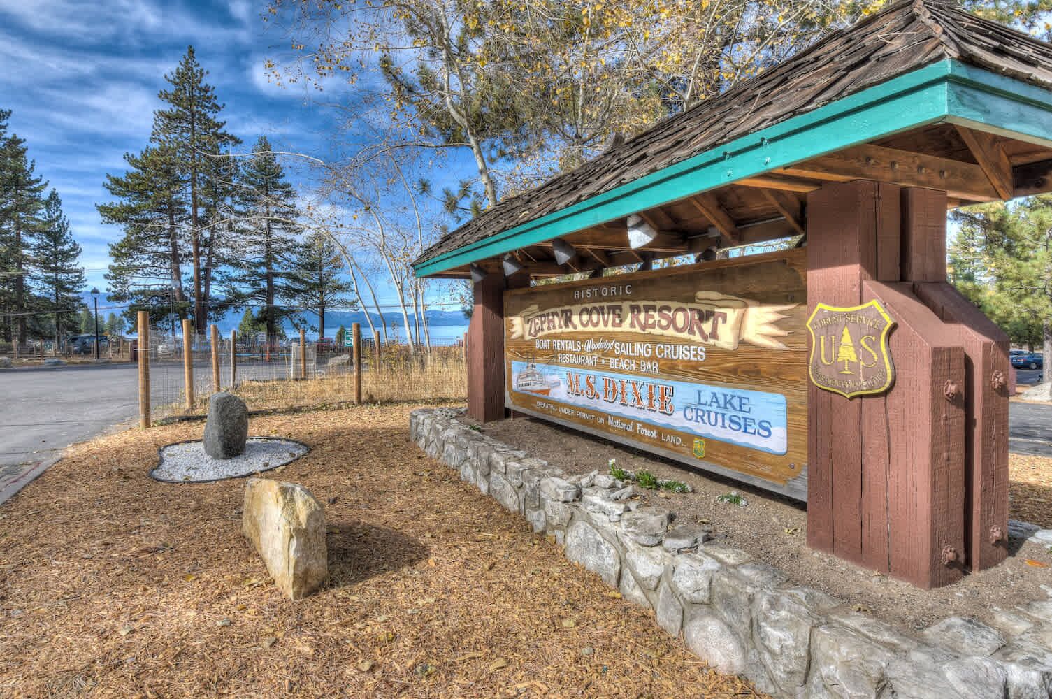 A wooden signboard with information about Zion Cove Resort, including amenities like boat rentals, sailing cruises, a restaurant, and a beach bar.