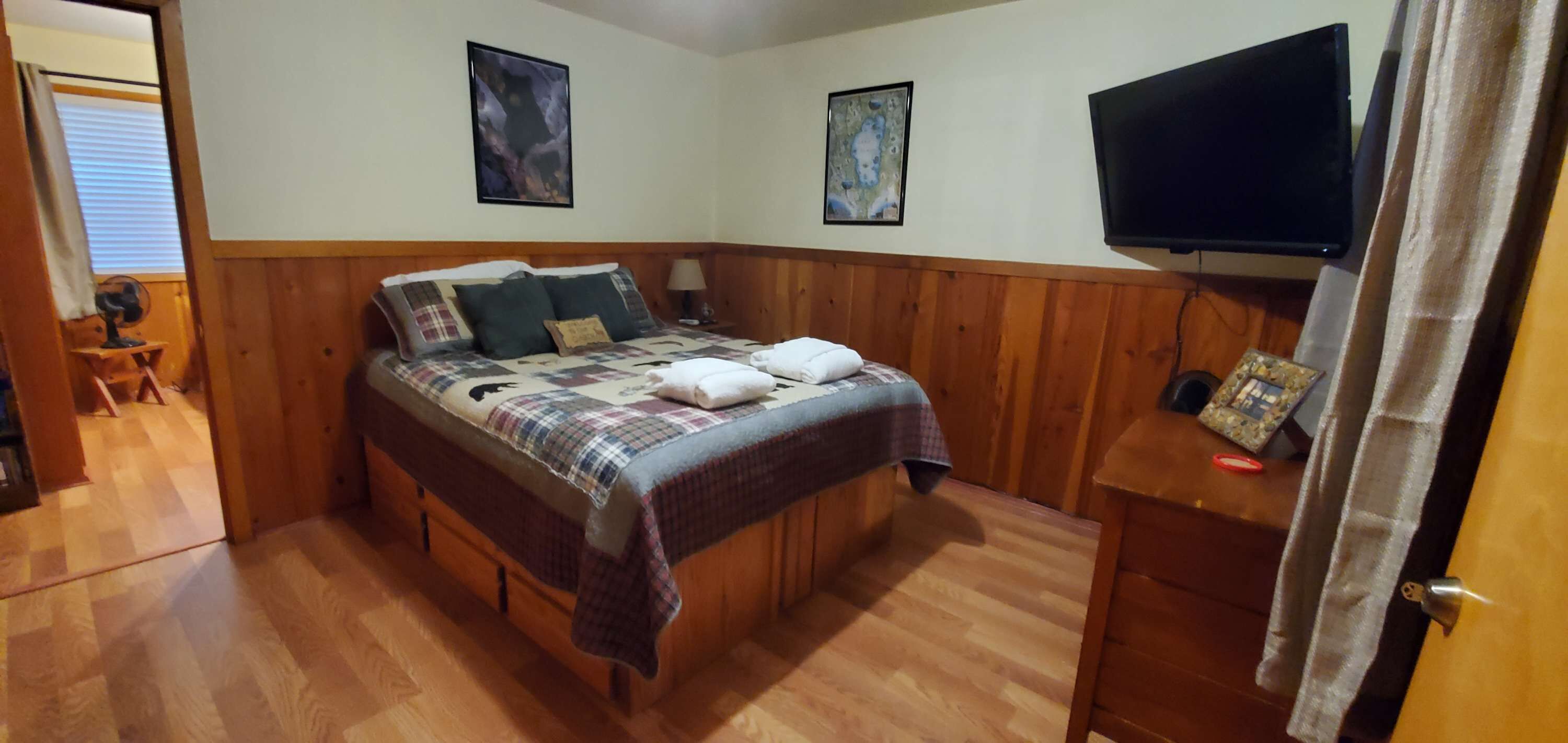 Une chambre à coucher avec un lit en bois, deux téléviseurs fixés au mur et une table de chevet avec une lampe.