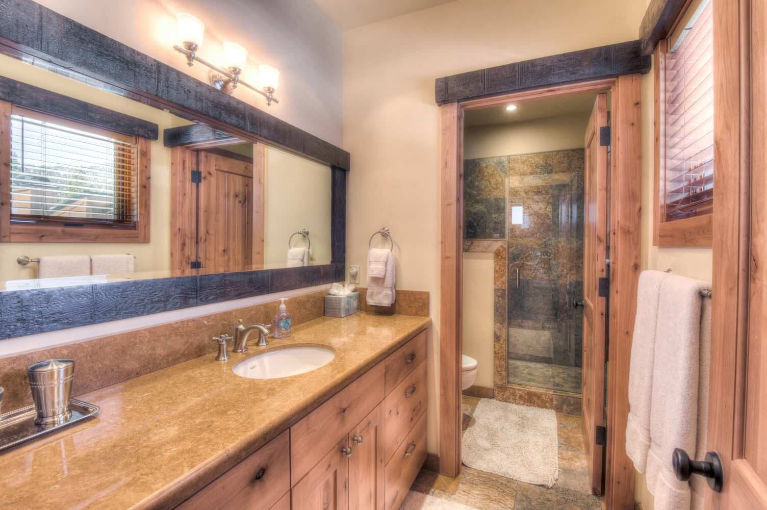 Un baño con dos lavamanos, un espejo grande, armarios de madera y cabina de ducha de vidrio.