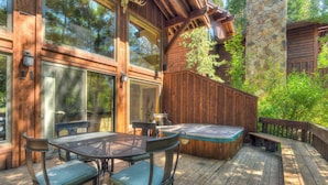 A wooden deck with a hot tub, outdoor seating, and a stone wall. - Ridge Court Barrel Relax in Private Hot Tub (Olympic Valley)