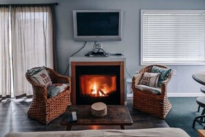 Una sala de estar con chimenea, dos sillones de mimbre, un televisor y una ventana con persianas.