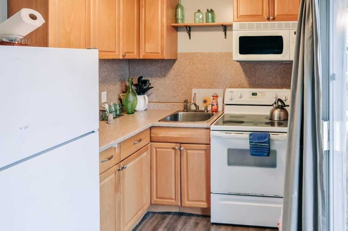 A compact kitchen with wooden cabinets, a white refrigerator, a microwave, a stove, and a sink.