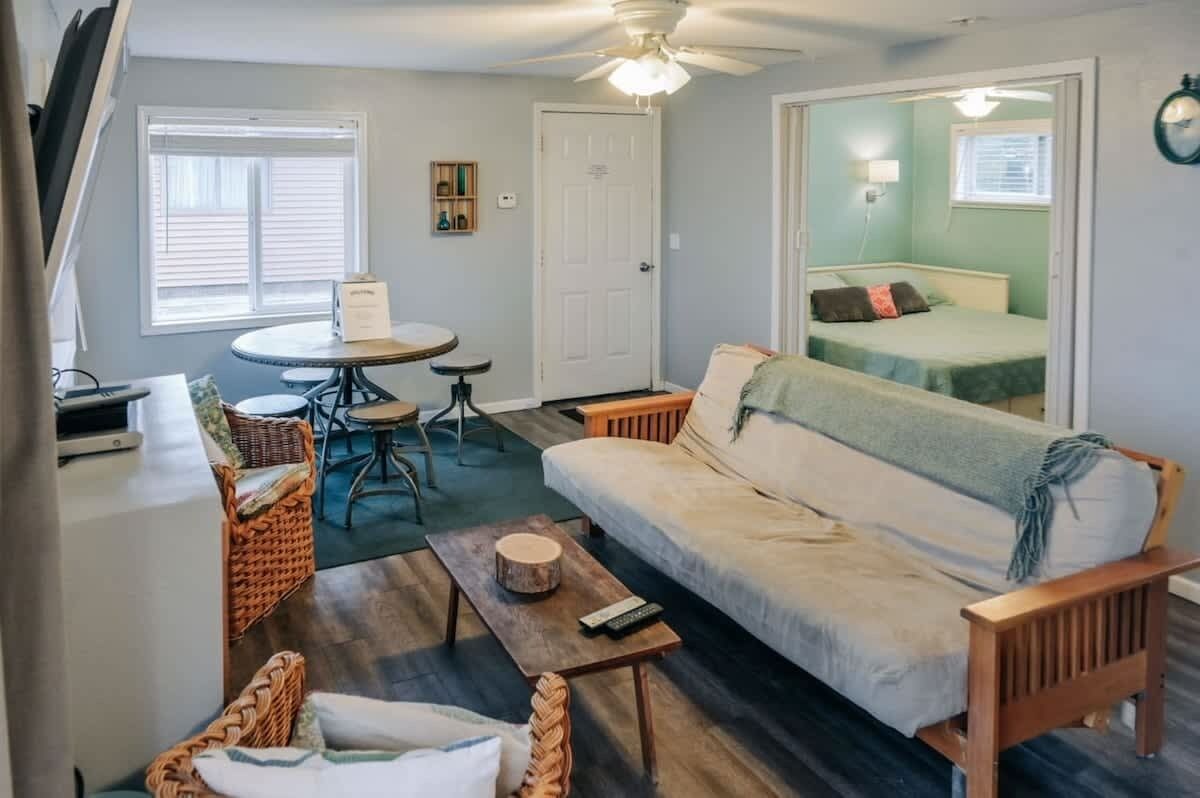 A compact living space with a sofa, a small dining table, a chair, a bed, and a ceiling fan.