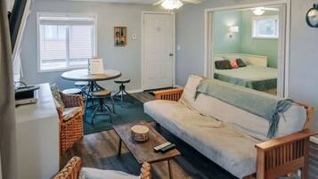 A compact living space with a sofa, a small dining table, a chair, a bed, and a ceiling fan.