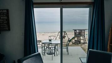 Una stanza con vista sulla spiaggia, arredata con un tavolo e sedie, un pontile in legno e un cartello con parole a tema spiaggia.