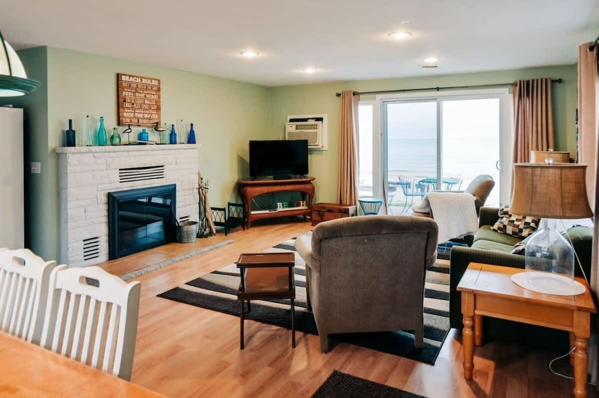 A living room with a fireplace, a television, and a view of the sea through a large window.