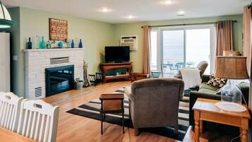 A living room with a fireplace, a television, and a view of the sea through a large window.